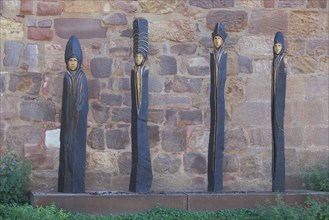 Four slender brown sculptures made of wood on the wall of the moated castle in Bad Vilbel