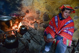 Quechua Indian in traditional dress cooking at the fireplace of his hut