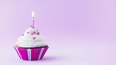 Birthday cupcake with illuminated candle purple background