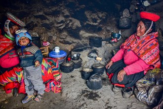 Quechua Indians in traditional dress cooking at the fireplace of their hut