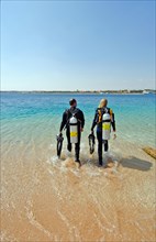 Young couple young man and young woman walking together with scuba diving equipment for scuba diving side by side across beach in Red Sea