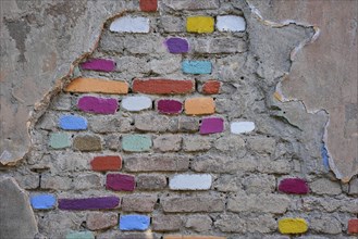 Wall with damaged plaster and colourfully painted bricks