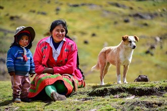 Quechua Indian family in traditional dress with dog sitting in a meadow