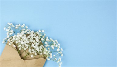 Brown envelop with small white gypsophila flowers arranged corner blue backdrop