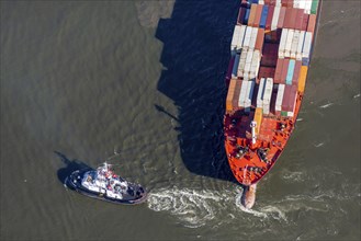 Aerial view of a tugboat pulling a container ship on the Elbe and giving direction