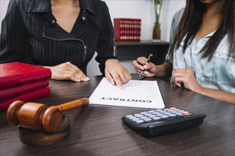 Black woman pointing document near lady with pen table with calculator gavel