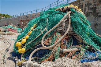 Fishing nets with yellow floats lie piled up up at the harbour pier