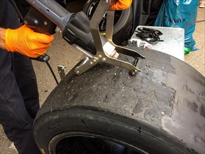 Race mechanic cleans surface of racing tyres slicks makes reconditioning spreads used tyres again for reuse at car races