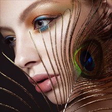 Beautiful girl with bright colored makeup and peacock feather on her face. Beauty face. Close-up. Photos shot in the studio