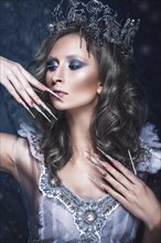 Beautiful girl in the image of the Snow Queen with creative make-up in a transparent dress with a crown and a long nail art. The beauty of the face. Photos shot in the studio