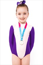Little girl gymnast with a medal in a sports swimsuit doing exercises. Photo taken in the studio on a white background