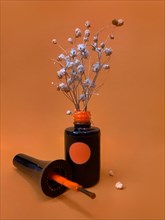 Black bottle of nail polish on a orange background with flowers. Manicure design