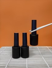 Black bottles of nail polish on a orange background. Manicure design
