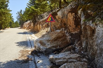 Triangular road sign Attention falling rocks huge boulder on the roadside