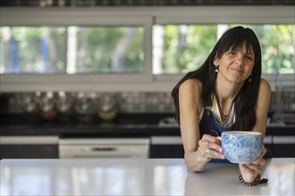 Portrait of a smiling woman enjoying a relaxing coffee break at home while looking at camera