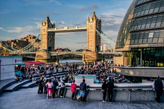 Spectators at The Scoop amphitheatre with London City Hall and Tower Bridge over the Thames in the evening sun