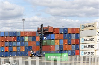 Containers stacked in piles lifted by toplifter machinery on quayside