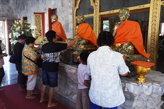 Believers cover statues of monks with gold leaf