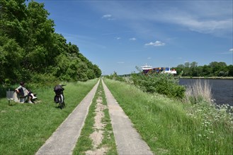 Woman sitting on a bench watching container ship on the cycle path from the Kiel Canal