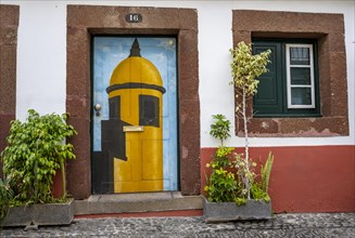 Colourfully painted door with tower of the Forte de Sao Tiago and plants on a house facade