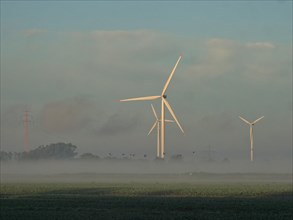 Wind turbines and power lines in the early morning fog. Ochsenwerder