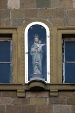 Figure of a saint on a house facade in a niche behind glass