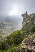 Female tourist looking over valley from cliff in the mist at the Macizo de Anaga national park on the island of Tenerife in the Canary Islands