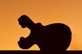 Wooden sculpture of African hippo with open mouth silhouetted against sunset