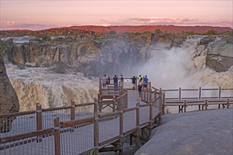 Western tourists watching waterfall from viewing platform at sunset in the Augrabies Falls National Park in the Northern Cape Province