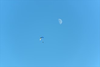 Paramotor in flight on a sunny day with the moon in the sky. France
