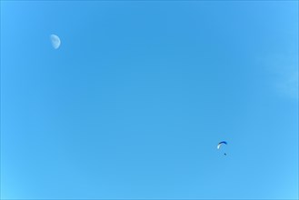 Paramotor in flight on a sunny day with the moon in the sky. France