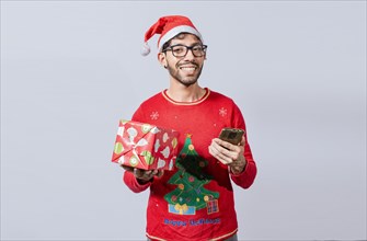 Handsome man in christmas hat holding gift and looking at phone