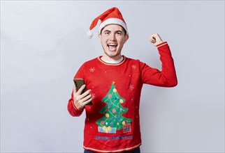 Happy smiling man in christmas hat holding cellphone celebrating