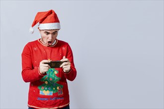 Guy in christmas hat looking at a christmas promo on phone. Surprised man watching a christmas promotion on the phone