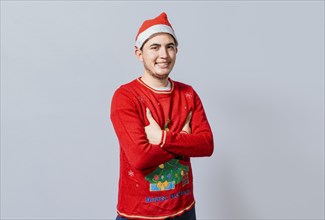 Portrait of guy in sweater and christmas hat with crossed arms isolated. Smiling guy in christmas hat with crossed arms smiling. Teenage guy in christmas clothes with crossed arms smiling