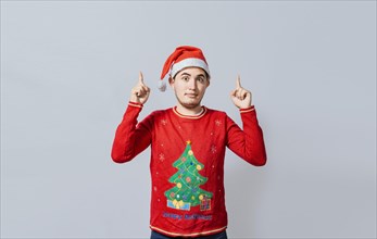 Guy in Christmas clothes pointing and recommending. Portrait of guy in sweater and christmas hat pointing up isolated. Caucasian young man in Christmas clothes pointing up an advertisement
