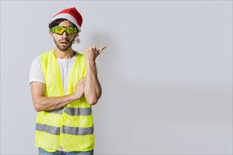 Amazed builder engineer in christmas hat pointing a copy space. Engineer man in christmas hat showing a product