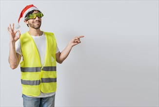 Engineer in christmas hat showing and recommending a product. Builder man in christmas hat pointing a christmas promo. Civil engineer in christmas hat recommending a christmas offer