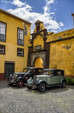 Vintage cars parked in front of yellow gate and wall