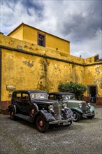 Vintage cars parked in front of yellow wall