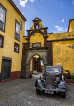 Vintage car parked in front of yellow gate and wall