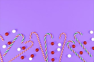 Christmas candy canes and ornament balls at bottom of purple background with copy space