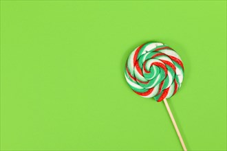 Lollipop with Christmas colors on green background with copy space
