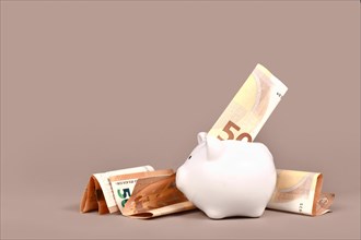 White piggy bank with 50 Euro bills on beige background with copy space. Concept for saving money