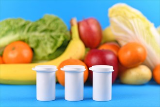 Bottles with food nutrition supplements in front of fruits and vegetables in blurry blue background