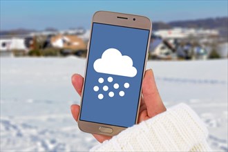 Winter snow weather forecast concept with hand holding mobile phone with snow icon in front of white snow landscape