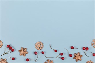 Seasonal flat lay with red winter berries and wooden snowflake Christmas ornaments at bottom of light blue background with empty copy space