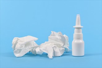 Nasal spray bottle and used tissues used during common cold on blue background