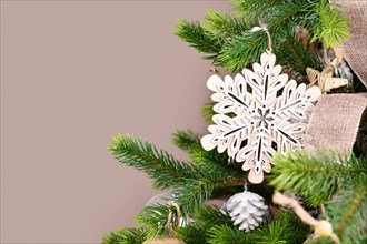 Christmas tree branch with natural wooden snowflake ornament in front of beige background with copy space