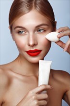 Beautiful girl with red lips and classic makeup with foundation and sponge in hand. Beauty face. Photo taken in the studio